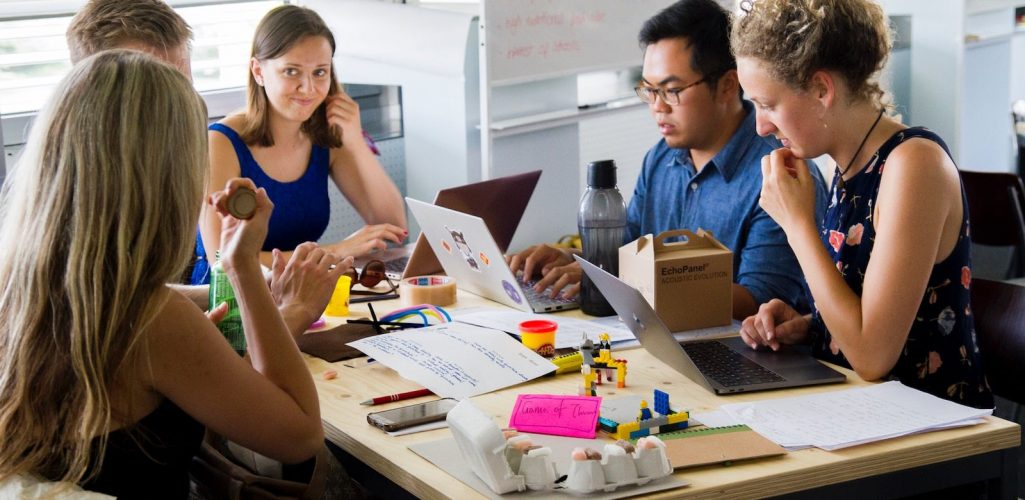 Photo of five people sitting at a worktable, using laptop computers